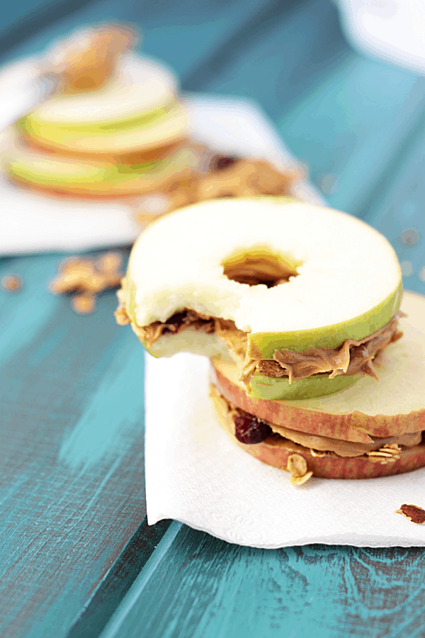 apple and peanut butter sandwiching granola on a blue wooden surface