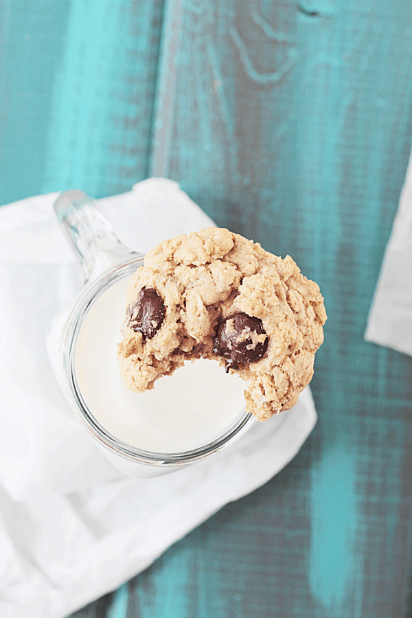 an oatmeal chocolate chip cookie with a bite taken out of it, resting on a jar of milk