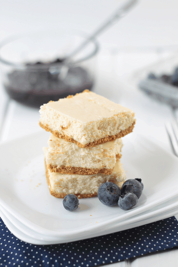 Lemon Cheesecake Bars stacked on top of each other with blueberries on the side