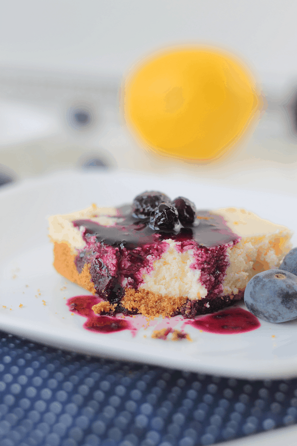 a lemon cheesecake bar with a bite taken out of it and blueberry topping drizzled on top 