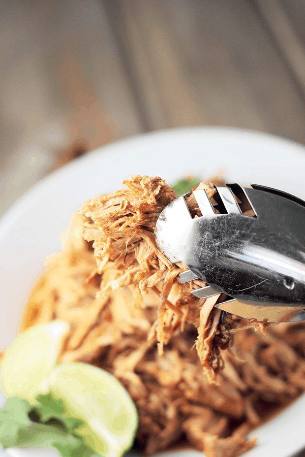 mexican pulled pork between tongs being added to a plate out of focus in the background