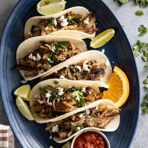 Overhead view of carnitas in tortillas all lined up on a blue plate.