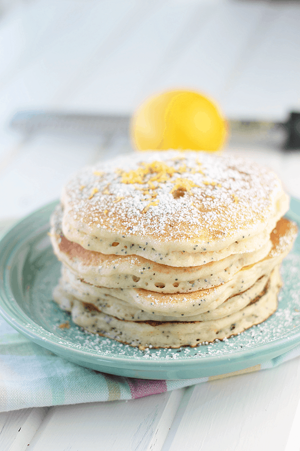 stack of lemon ricotta pancakes on a blue plate with powdered sugar and lemon zest on top