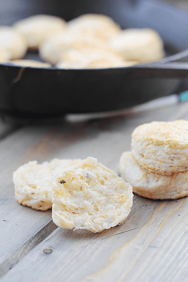 rosemary cheddar biscuits in the foreground with one halved, and the rest out of focus in the background in a bowl