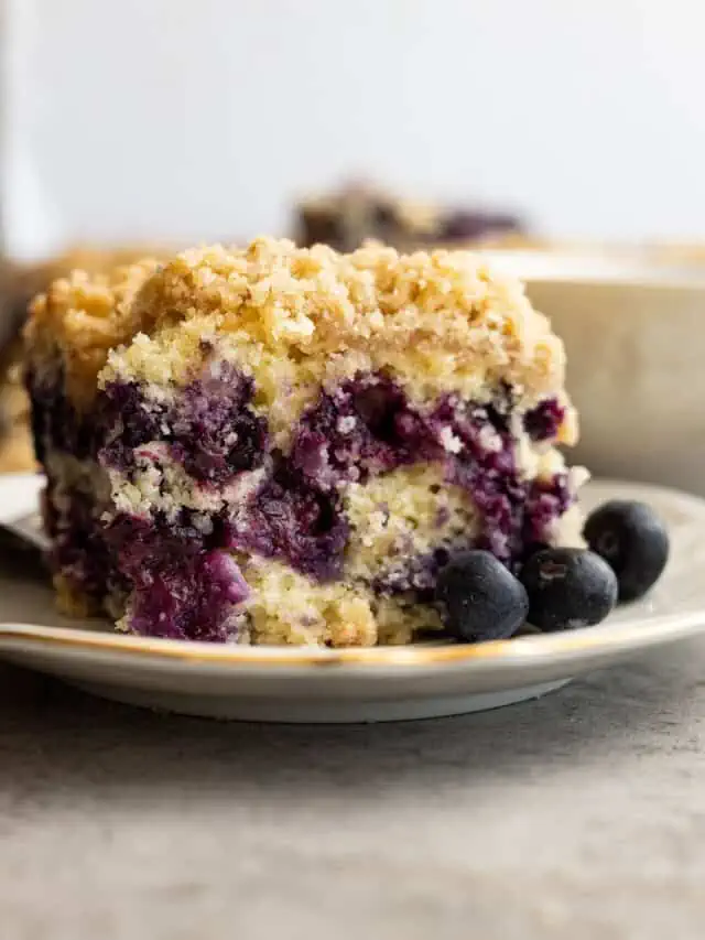 Blueberry buckle on a plate with blueberries off to the side.