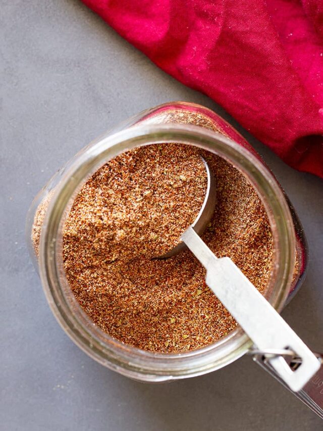 Top down of taco seasoning in a jar with a measuring spoon in it.