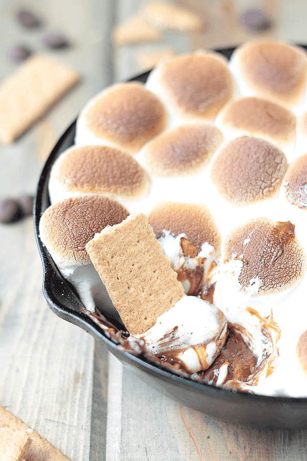 a black cast iron skillet full of toasted marshmallows on top of a s'more's dip and a graham cracker dipping into it