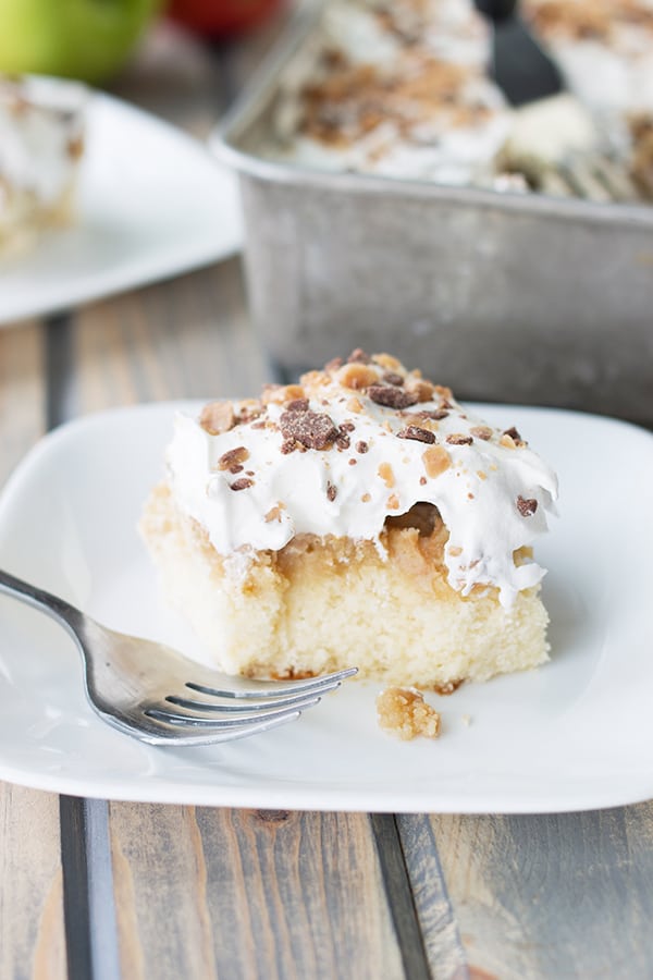 a cut square of caramel apple cake with a bit taken out of it on a white plate with a fork resting on it
