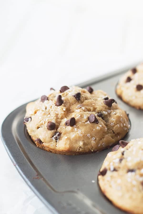 a muffin tin with peanut butter chocolate chip muffins inside, this photo focusing exclusively on one muffin the corner garnished with extra mini chocolate chips and coarse sugar crystals