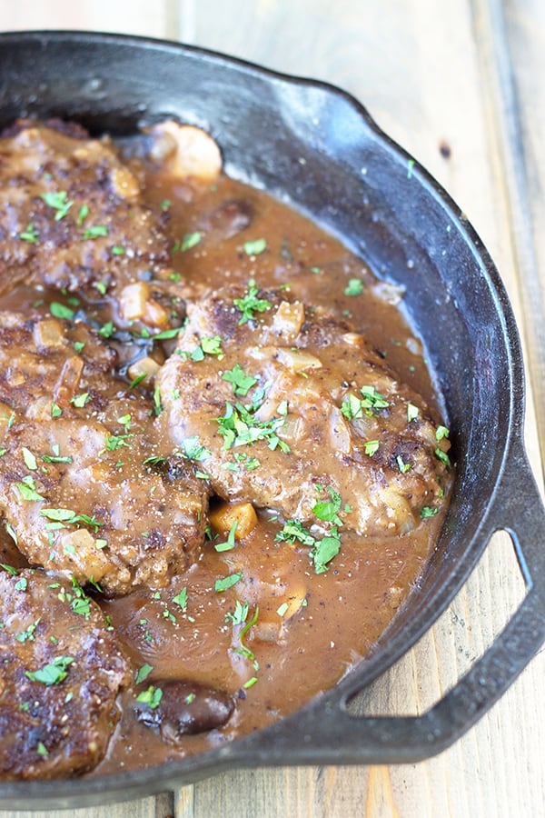 salisbury steaks in an onion gravy sauce with garnish in a cast iron skillet