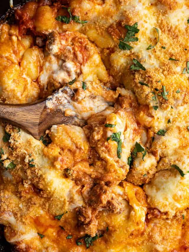 Overhead view of baked gnocchi with a spoon in the middle showing how gooey the casserole is.