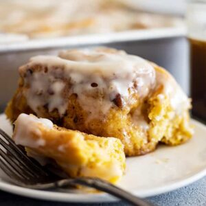 Straight on view of a pumpkin cinnamon roll with a fork off to the side. Can see the frosting dripping off the sides.