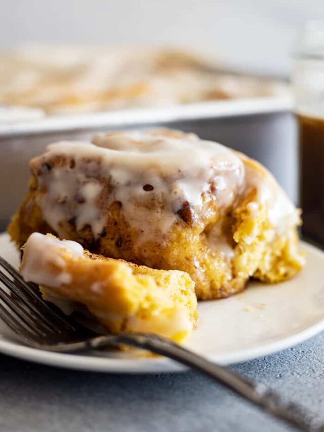 Straight on view of a pumpkin cinnamon roll with a fork off to the side. Can see the frosting dripping off the sides.