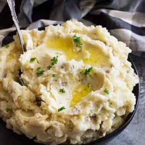 Large bowl of slow cooker mashed potatoes topped with butter and chopped parsley to garnish.