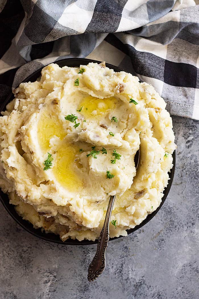 Large bowl of slow cooker mashed potatoes with pools of melted butter and chopped parsley for garnish.