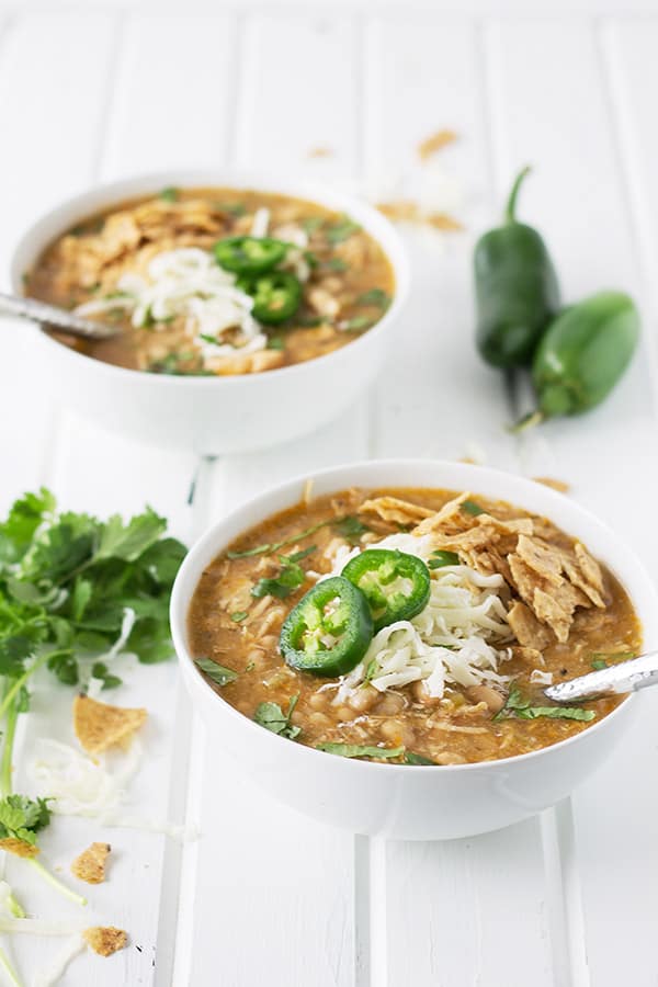 two bowls of white chicken chili garnished with cheese and jalapeno