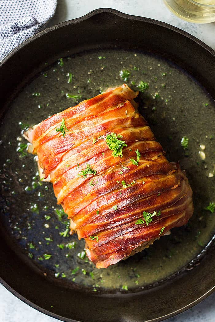 Pork loin wrapped in bacon in a cast iron skillet.