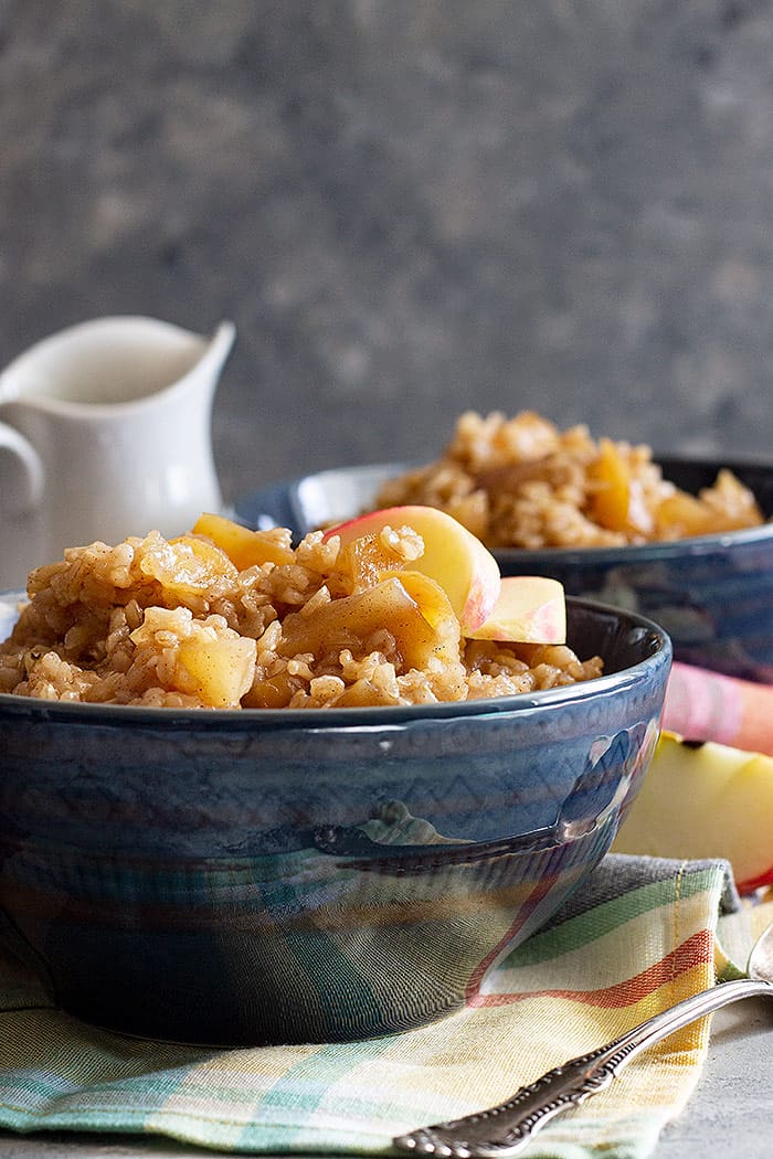 Two bowls of Slow Cooker Cinnamon Apple Breakfast Rice garnished with fresh apples. 