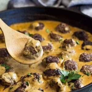 Pan of swedish meatballs with a spoon lifting one out.