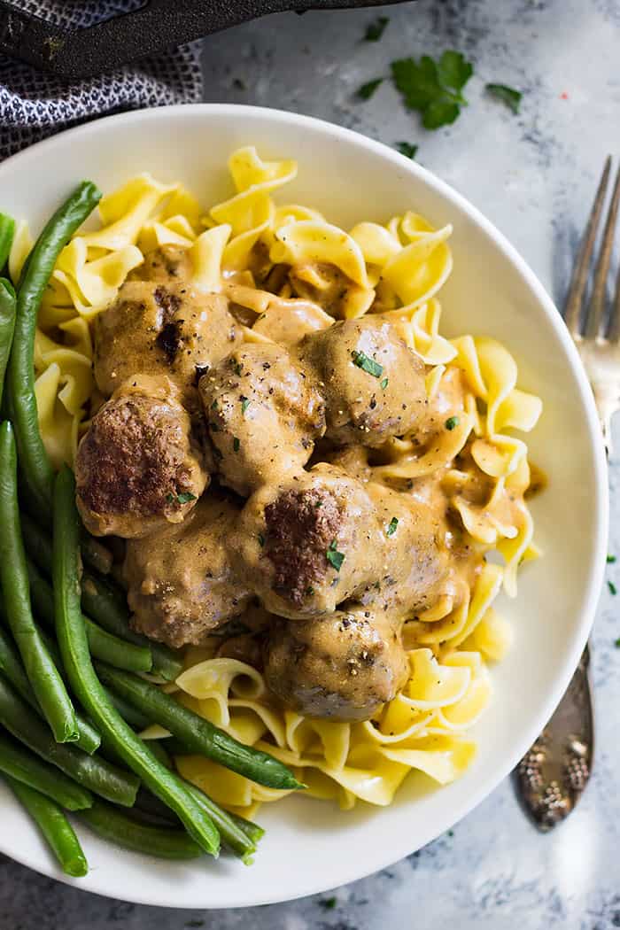 A big bowl of egg noodles topped with Swedish meatballs and a side of green beans. 