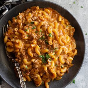 A plate piled high with hamburger helper and garnished with parlsey.