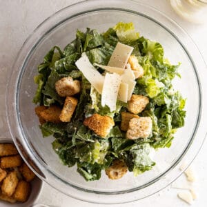 Overhead view of caesar salad in a bowl dressed with dressing, parmesan, and croutons.