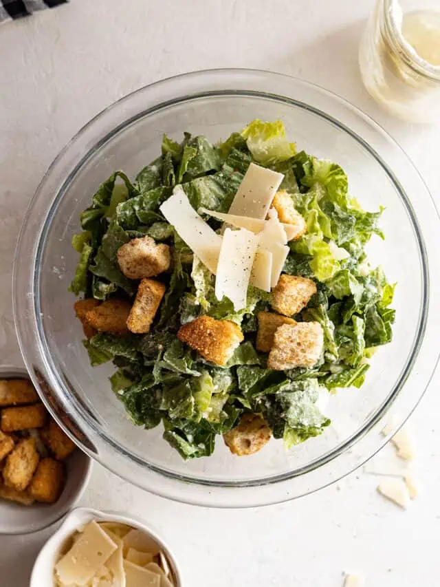 Overhead view of caesar salad in a bowl dressed with dressing, parmesan, and croutons.