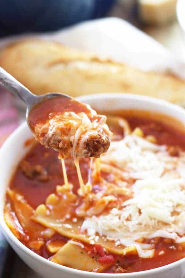a bowl of lasagna soup with a spoon lifting a bite out of the bowl 