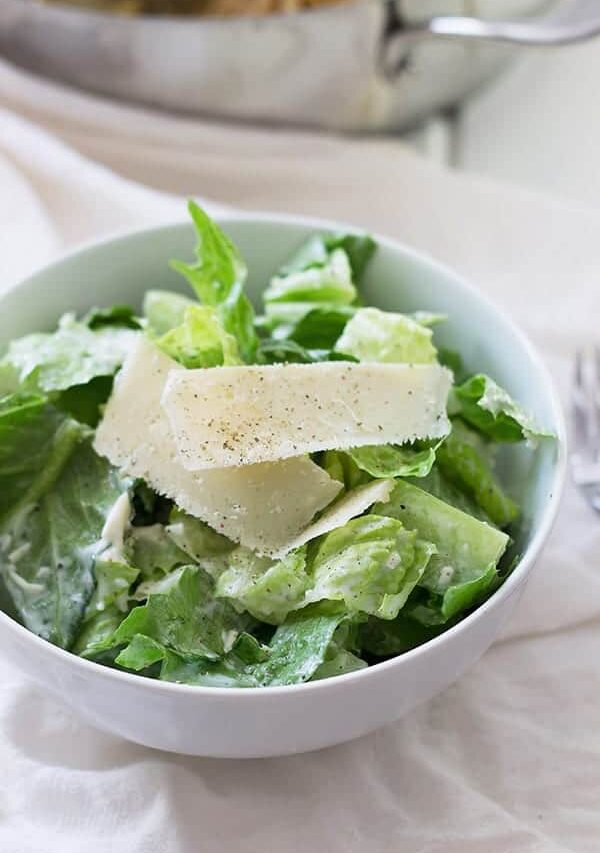 Caesar salad in circular white dish with shredded parmesan on top.