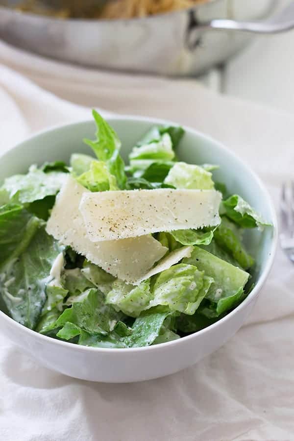 Caesar salad in circular white dish with shredded parmesan on top. 