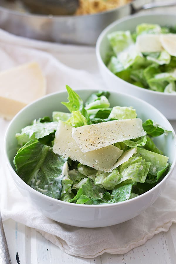 Simple Caesar salad in circular white bowl with fresh Parmesan. 