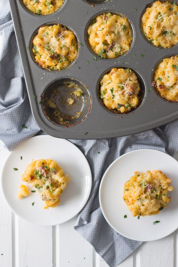 Macaroni and Cheese cups, baked in a muffin tin with two removed and on two circular white plates. 