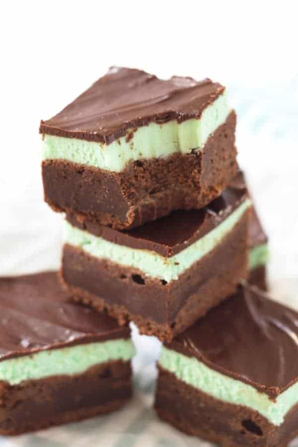 A stack of mint chocolate brownies. There are 4 brownies shown and the one on top has a bite taken out of it.