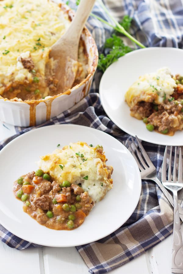 a casserole dish full of shepherd's pie and two plates with a serving on them