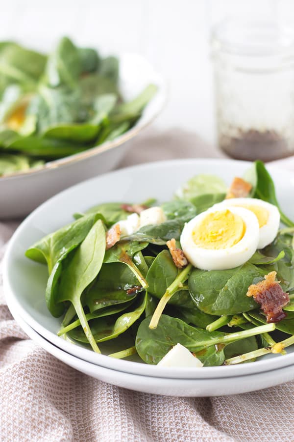Side view of warm spinach salad with bacon in a circular white plate. 