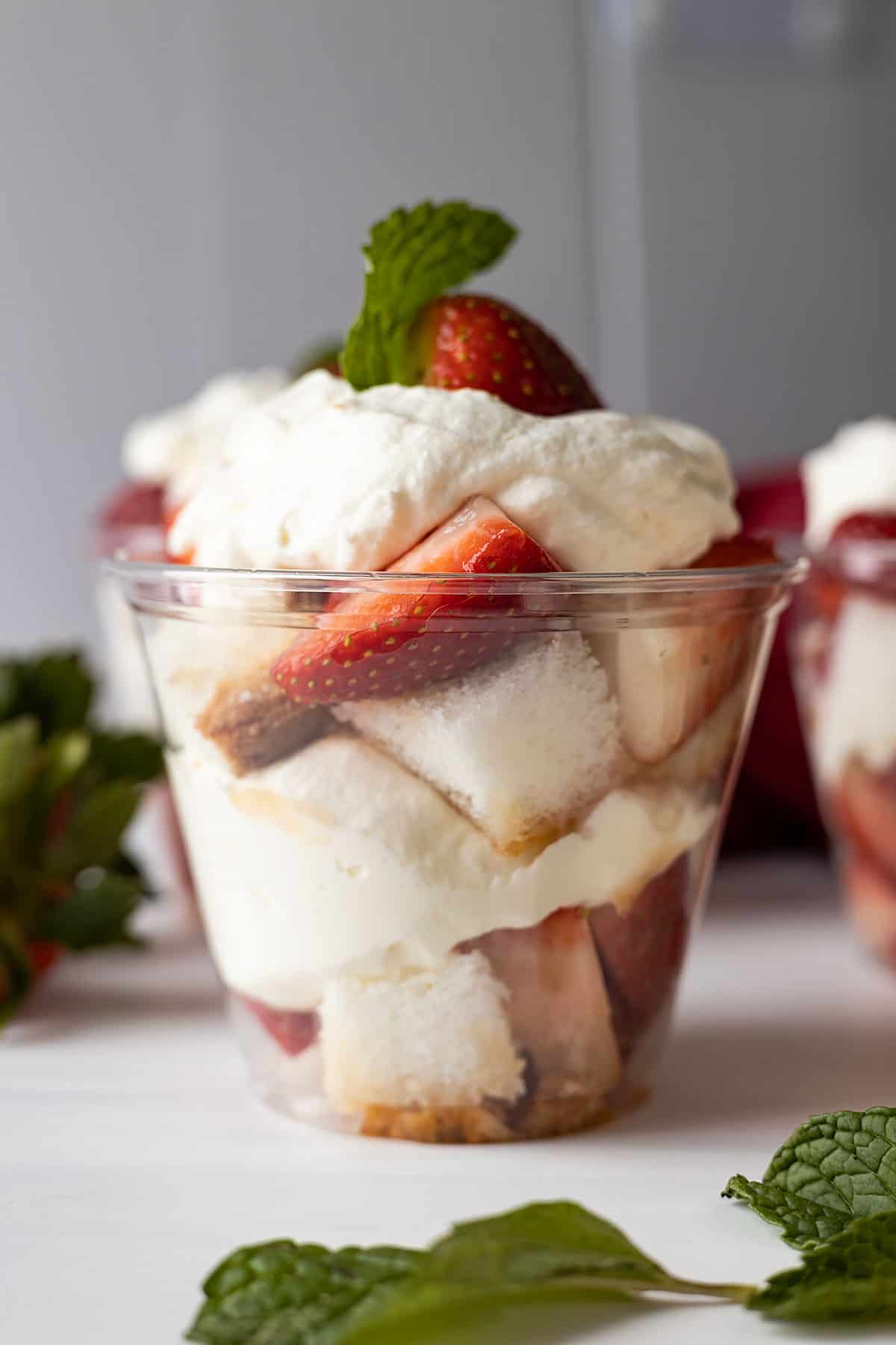 A clear plastic cup layered with angel food cake cubes, fresh strawberries, and freshly whipped cream.