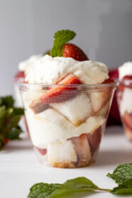 Straight on shot of strawberry shortcake cup. Garnished with mint and mint and strawberries scattered around cup.