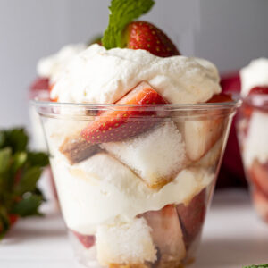 Straight on shot of strawberry shortcake cup. Garnished with mint and mint and strawberries scattered around cup.