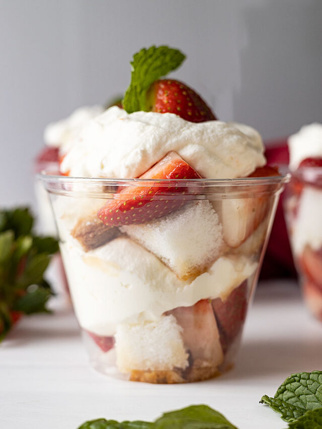 Straight on shot of strawberry shortcake cup. Garnished with mint and mint and strawberries scattered around cup.