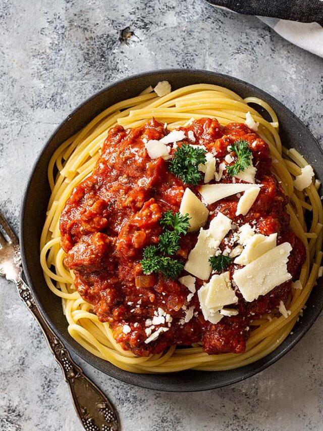 Top down view of spaghetti sauce over noodles and topped with cheese.