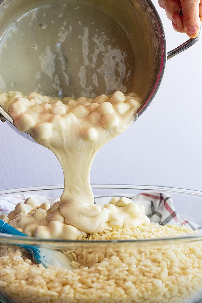 A large pan of melted mashmallows being poured into a bowl of rice krispies. 