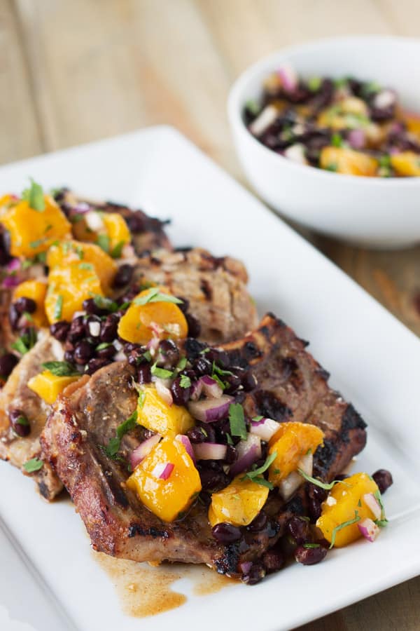 grilled citrus marinated pork chops topped with mango and black bean salsa on a white plate
