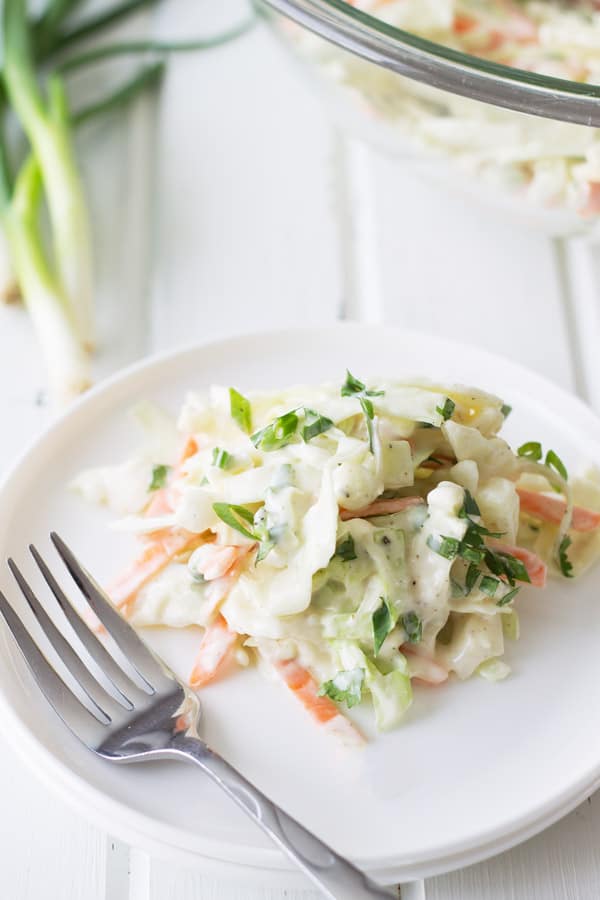 Shredded cabbage and carrot coleslaw on white plate next to fork.