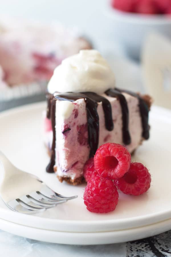 close up shot of triple berry frozen cheesecake with raspberries, hot fudge, and whipped cream garnishing it