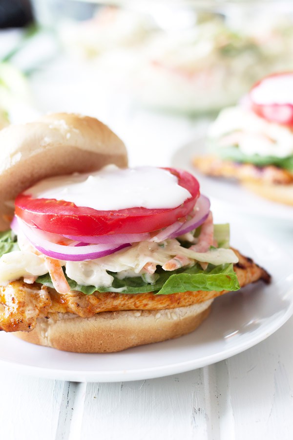 Grilled buffalo chicken sandwich topped with lettuce, tomato, creamy coleslaw, and onion on a bun.