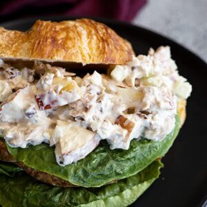Apple tuna salad piled on a buttery croissant with a leaf of lettuce..