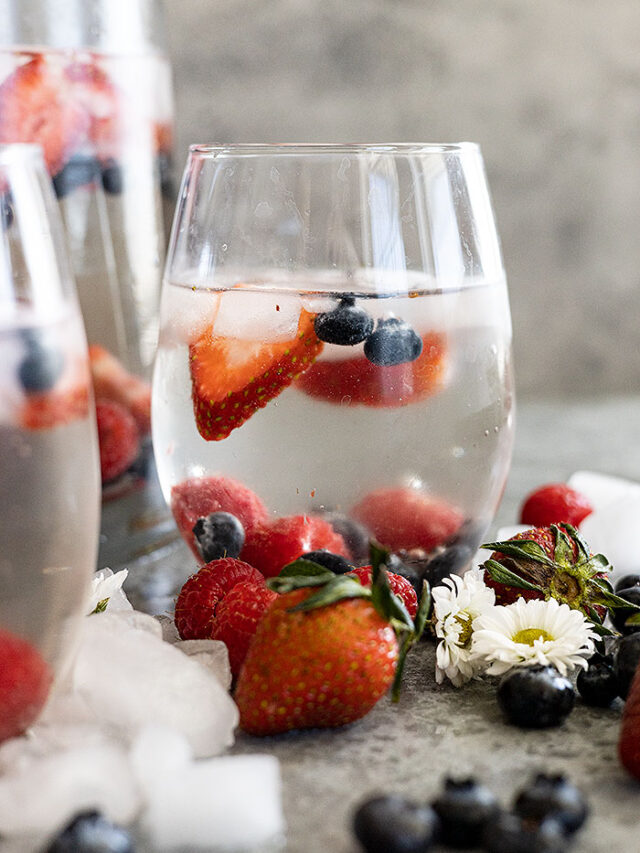 A glass of easy white sangria ready to drink. Ice cubes and fresh fruit all around the glas.