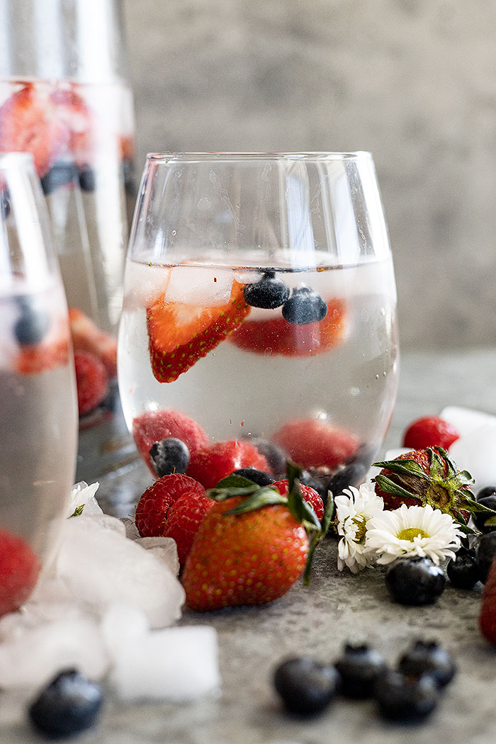 A glass of easy white sangria ready to drink. Ice cubes and fresh fruit all around the glas.
