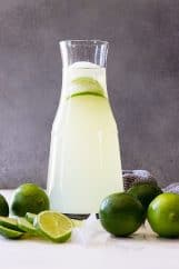 A tall pitcher of limeade with fresh limes as garnish.