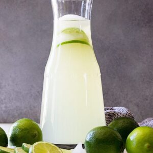 A tall pitcher of limeade with fresh limes as garnish.